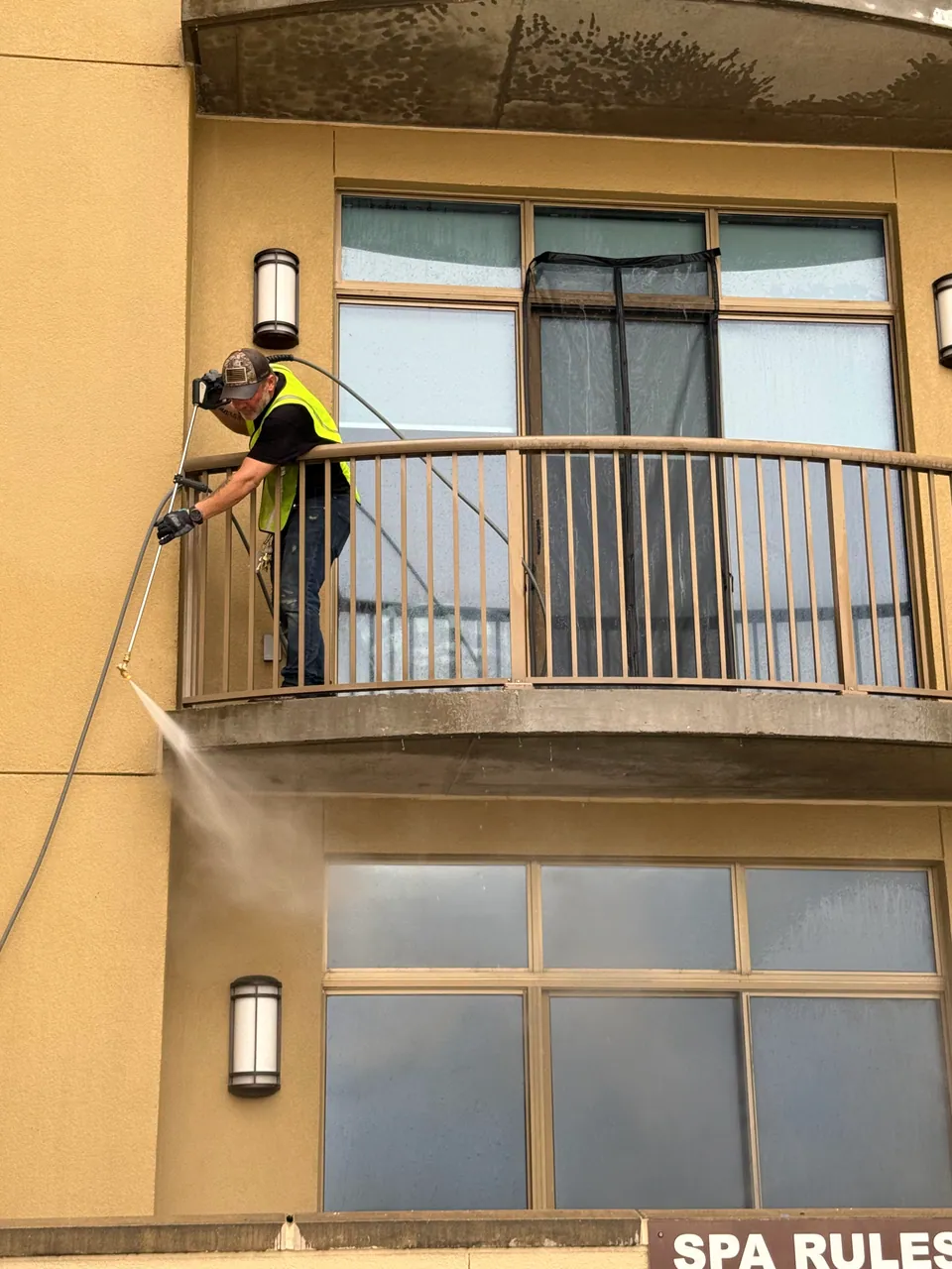 Operator cleaning a balcony exterior with the wand and water spray visible