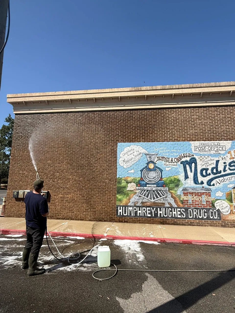 Operator washing a brick exterior beside a painted mural